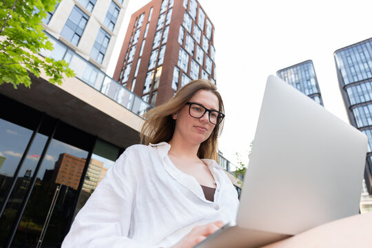 A woman works on her laptop outside a modern apartment building