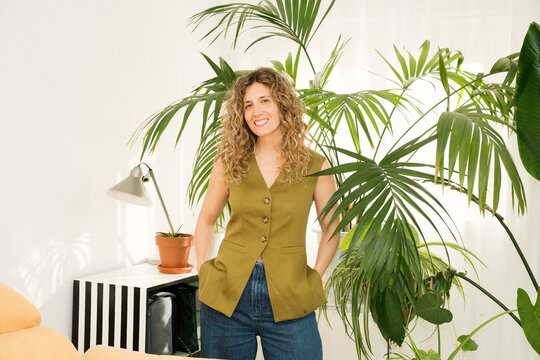 A woman stands on her sunny balcony surrounded by various houseplants