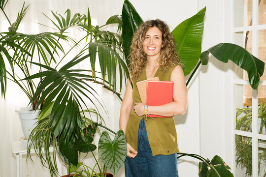 Woman holding notebooks in cozy balcony garden with houseplants