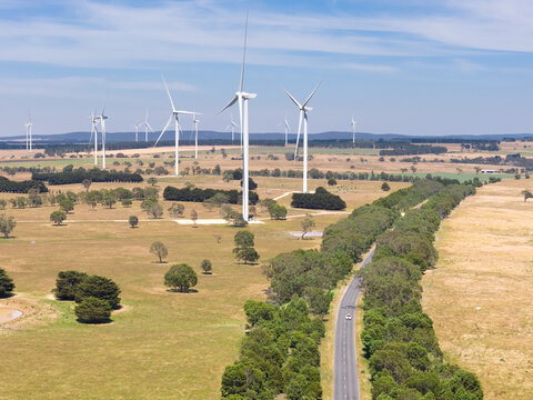 A country road near wind turbines on dry farmland against a blue sky