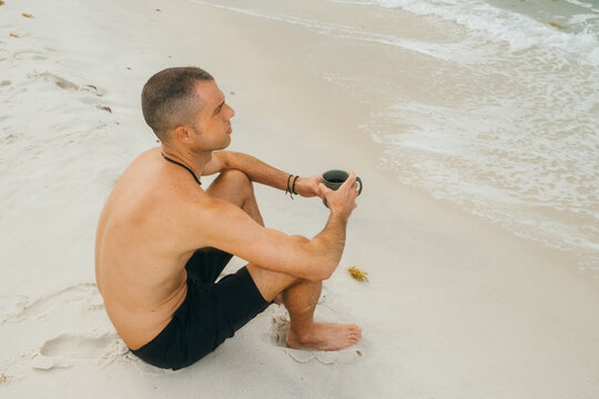 Man Sitting on Beach With Coffee Mug