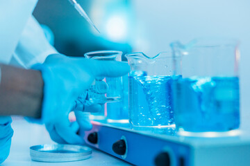 Fototapeta premium Gloved Lab Technician Positions Glass Beakers Filled with Vivid Blue Solution on Stirring Platform 