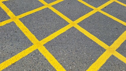 Fototapeta premium A yellow grid applied to a gray road surface. This markup illustrates the regulation of traffic flow and the concept of systematic order