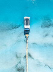 Fototapeta premium Top down aerial view of passenger ship yacht at wooden pier in Mallorca, Spain. Cruise boat docked at jetty in clear turquoise sea water near sandy beach. Drone tropical exotic summer landscape