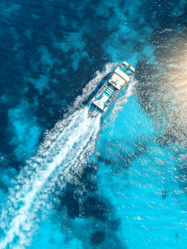 Top down aerial view of tourist catamaran boat cruise in turquoise sea water in summer. Mallorca island, Spain. Yacht moving fast with white foam wake trail. Mediterranean sea. Drone landscape. Ocean