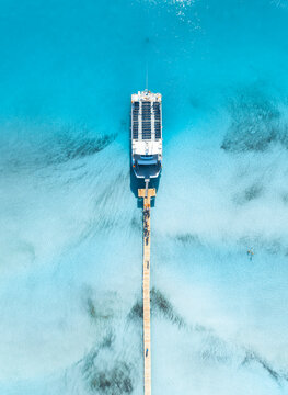 Top down aerial view of passenger ship yacht at wooden pier in Mallorca, Spain. Cruise boat docked at jetty in clear turquoise sea water near sandy beach. Drone tropical exotic summer landscape