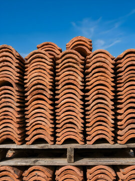 Stacked terracotta roof tiles on wooden pallet against clear blue sky