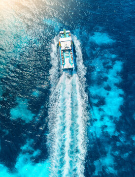 Top down aerial view of tourist catamaran boat cruise in turquoise sea water in summer. Mallorca island, Spain. Yacht moving fast with white foam wake trail. Mediterranean sea. Drone landscape. Ocean