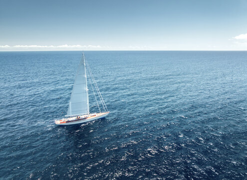 Aerial drone view of luxury sailing yacht moving in blue sea. Summer vacation and travel. Top view of modern sailboat cruising in Mediterranean sea. Yachting in Mallorca, Balearic island, Spain.