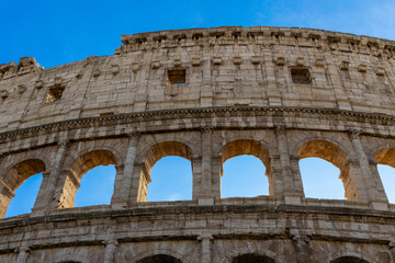 Obraz premium Famous Coliseum in Rome. Colosseum, or Coliseum. Part of the wall of an antique stone structure with arches. Italy, Europe. Famous touristic place in the world, Europe. Beautiful blue sky background.