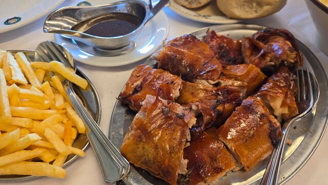 Traditional Portuguese meal with roasted suckling pig and creamy mushroom risotto served in a restaurant. Concepts: local cuisine, gastronomy, travel, culture, and dining.