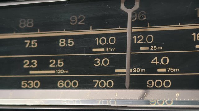 Macro shot of scanning for radio stations on a vintage analog tuner. The dusty frequency scale with off-white numbers highlights the classic 1980s receiver design.