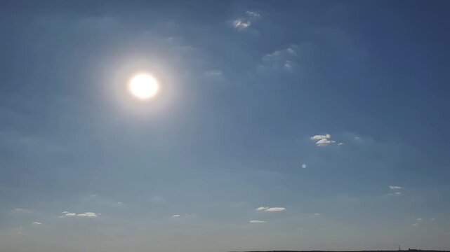 Wide panoramic shot of a single bird flying across a bright blue sky with scattered white clouds. The sunny atmosphere and open space emphasize concepts of freedom and nature.