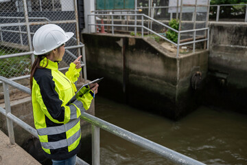 Fototapeta premium Professional female environmental engineer holding a clipboard inspecting wastewater drainage infrastructure at an industrial facility ensuring safety and sustainable public water management.