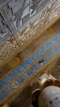 Dendera temple or Temple of Hathor. Painted columns with goddess faces and hieroglyphic ceiling of the hypostyle hall, ancient sandstone architecture with detailed carvings and blue painted astronomic