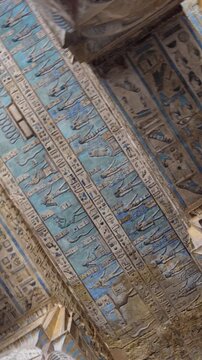 Dendera temple or Temple of Hathor. Painted columns with goddess faces and hieroglyphic ceiling of the hypostyle hall, ancient sandstone architecture with detailed carvings and blue painted astronomic