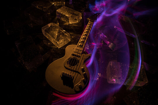 Music Concept: Guitar Miniature on a Dark Background with Vivid Light, Smoke, and Fire Effects. Golden electro guitar under a Dramatic Spotlight.