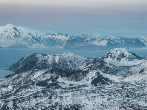 Aerial view of the snow-covered Aleutian mountain range and rugged coastline in Unalaska, Alaska, United States.
