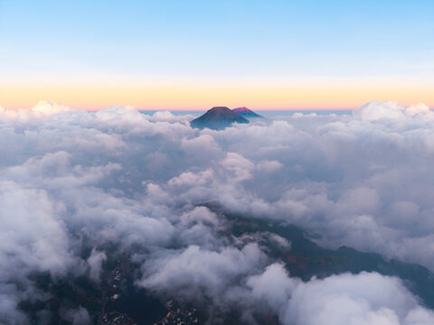 Aerial view of Sikunang mountain peaks rising above a dense sea of clouds during golden hour in Kejajar, Central Java, Indonesia.