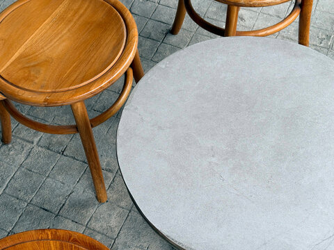 Modern Cafe Patio Furniture Set Top View Featuring Round Grey Terrazzo Stone Table and Vintage Wooden Stools on Textured Cobblestone Concrete Pavement Background for Interior Design Concept.