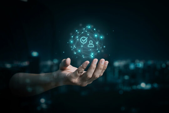​Hand holding glowing digital network sphere with user profile and checkmark icons against blurred night city lights in the background.