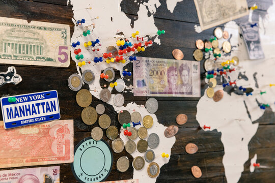 Travel Destinations Tracked on a Wooden Wall Map with Multi-colored Pins, Cash Bills and Collectible Coins.