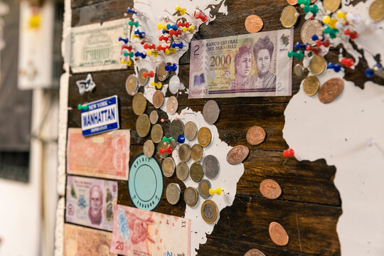 Travel Destinations Tracked on a Wooden Wall Map with Multi-colored Pins, Cash Bills and Collectible Coins.