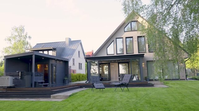 Modern Scandinavian house with large windows and outdoor seating area, showcasing a stylish black cabin in a lush green garden