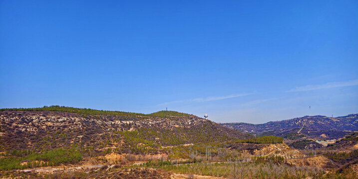 Panoramic dry hillside landscape with sparse forest under clear blue sky