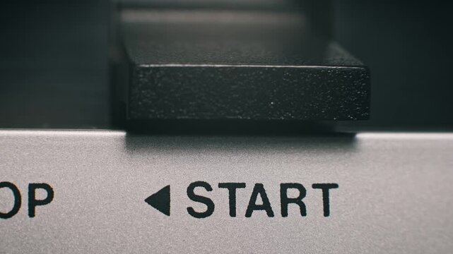 Extreme close-up of a finger pushing a black textured start button on a vintage silver tape player. This analog technology features a classic user interface and mechanism.