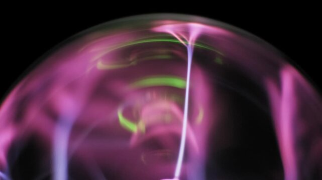 Top-down view of a plasma globe with pink and purple bolt arcs moving from a central electrode inside a glass sphere. Flowing ionized gas tendrils create a dynamic science display.