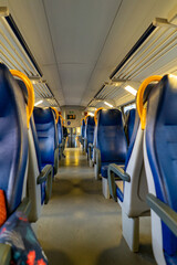 Fototapeta premium The perspective shot shows rows of empty blue seats with yellow grab handles inside a passenger train carriage, illuminated by overhead lights