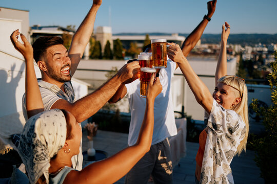 Cheering friends toasting beer on rooftop celebration