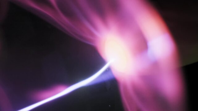Side view of a finger touching a plasma ball glass sphere where a single bright electric arc follows the fingertip. Pink and purple ionized gas tendrils move inside.