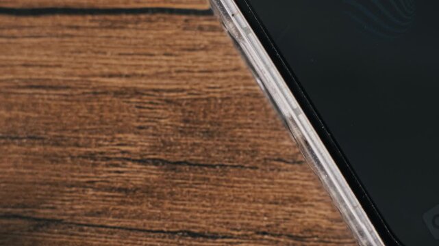 Angled close-up of a hand unplugging a white USB-C power cord from a smartphone on a textured wood surface. The device in a transparent protector case disconnects from the supply.