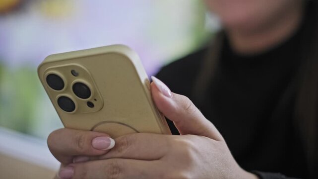Close-up shot of female hands with a French manicure holding a modern smartphone in a yellow case. The camera slowly zooms in on the multiple lenses on the back.