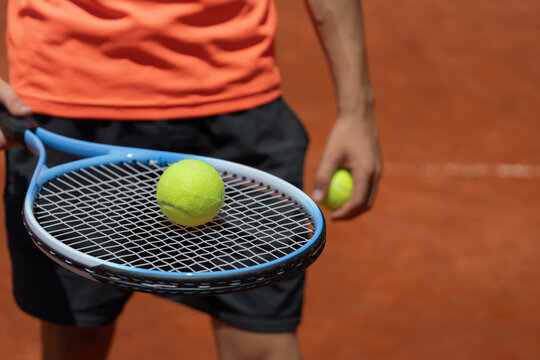 Tennis player holding racket with tennis ball and second ball in hand on clay court. Horizontal composition with copy space, ideal for sports, training and competition concepts
