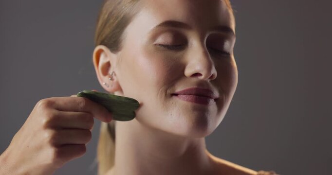 Smile, skincare and woman in studio with gua sha for natural beauty, massage and luxury cosmetics. Dermatology, facial care and girl with confidence, jade stone and healthy skin on grey background.