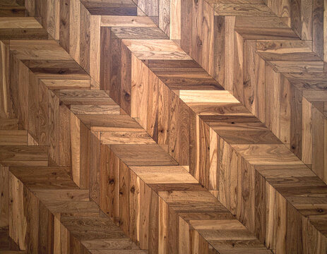 A close-up view of an intricately patterned wooden floor with herringbone tiles, showcasing natural wood grain variations and warm brown tones.