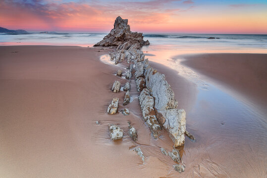 Beautiful long exposure seascape of flysch rock formations at Sopelana beach during a colorful sunset with silky water in the Basque Country, Spain