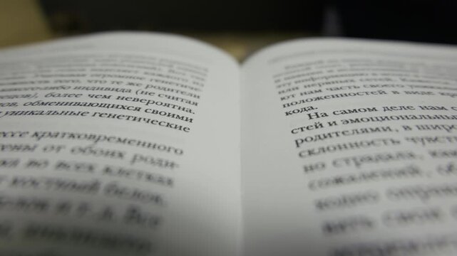 A close-up shot focuses on an open book displaying Cyrillic text on white pages. The camera gradually pulls focus, revealing printed Russian words within a very shallow depth of field,