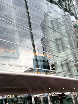 Modern glass skyscraper facade reflecting surrounding city buildings and sky