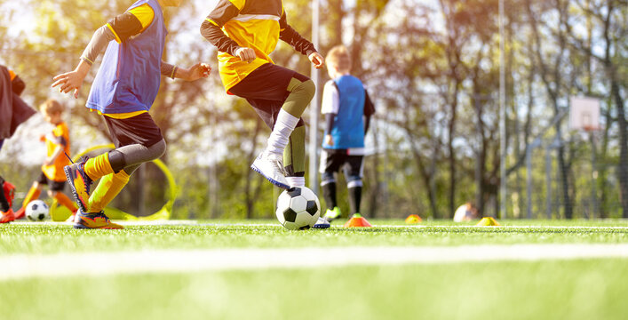 Youth Soccer Training Drill: Low Angle View of Kids Running with Ball on Pitch. Kids Soccer Match Action: Dynamic View of Junior Footballers Running on Green Grass Field