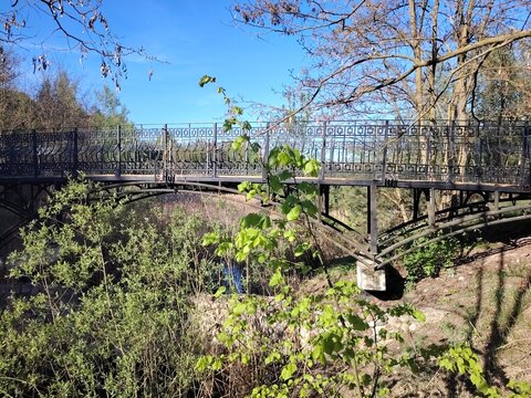Arched metal pedestrian bridge in a green park on a bright sunny day
