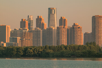 Modern city skyline at sunset above lakeside trees © PhungBao