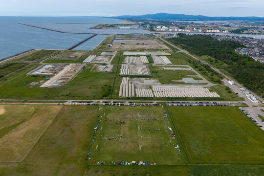 Aerial view of Kenmin Seaside Park featuring a large sports field with people, rows of concrete tetrapods, coastal breakwaters, and green space in Kanazawa, Ishikawa, Japan.