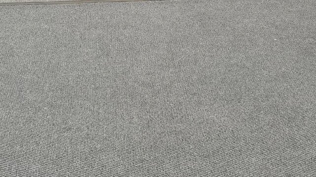 Low angle slow motion of people wearing white sneakers and casual pants walking, stepping, and shuffling on a grey textured carpet floor