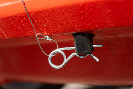 Metal cotter pin fastener attached to a safety wire cable holding a locking pin mechanism in place on an orange red industrial hull