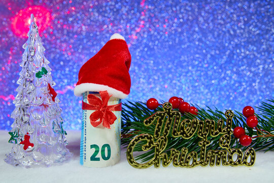 On a blue background, next to Christmas tree branches with letters, is a decorated euro banknote with a Christmas tree