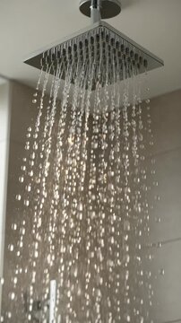Water drops falling from a modern square rainfall shower head in a stylish bathroom, representing hygiene, relaxation, and wellness in a close-up, slow-motion shot
